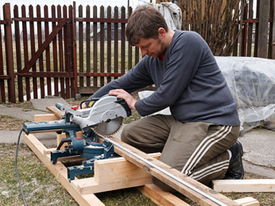 Ein Mann benutzt eine Gehrungssäge, um ein Holzstück auf einer Baustelle zu schneiden.